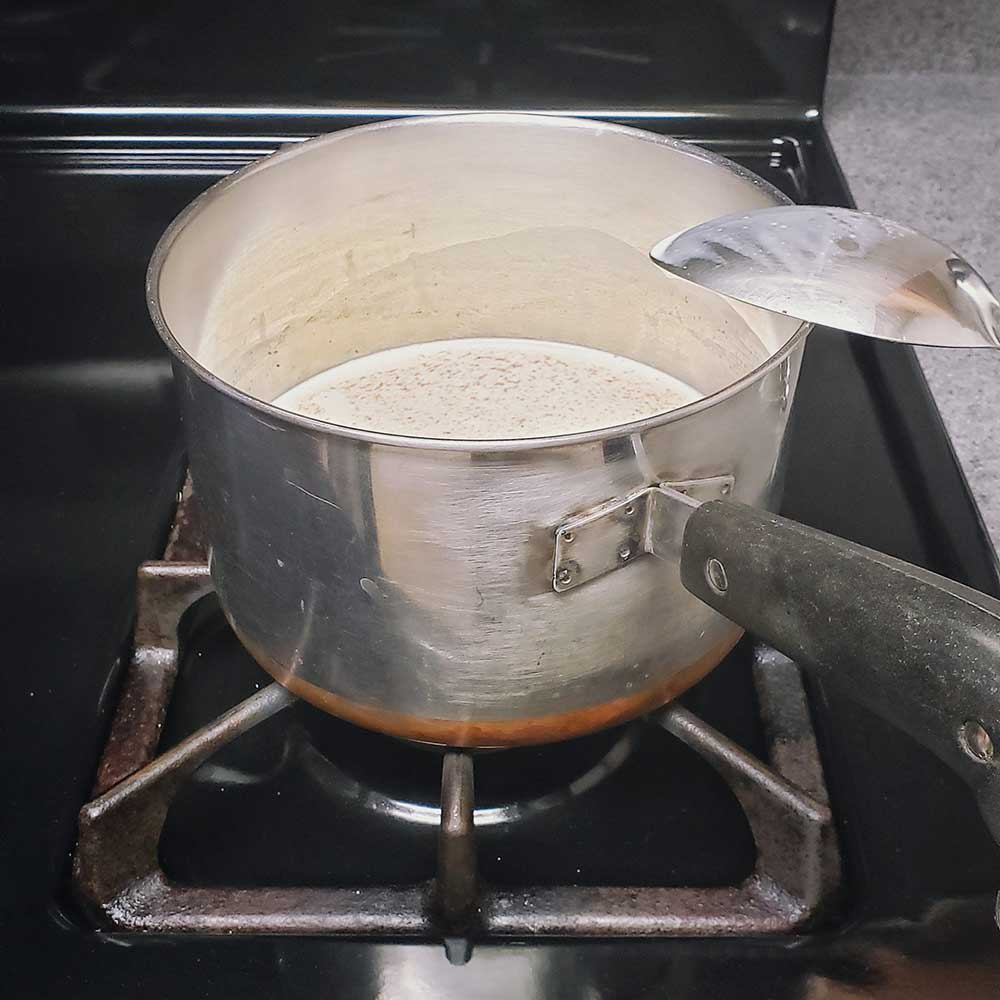 A saucepan on a stove filled with milk, heavy whipping cream and nutmeg.