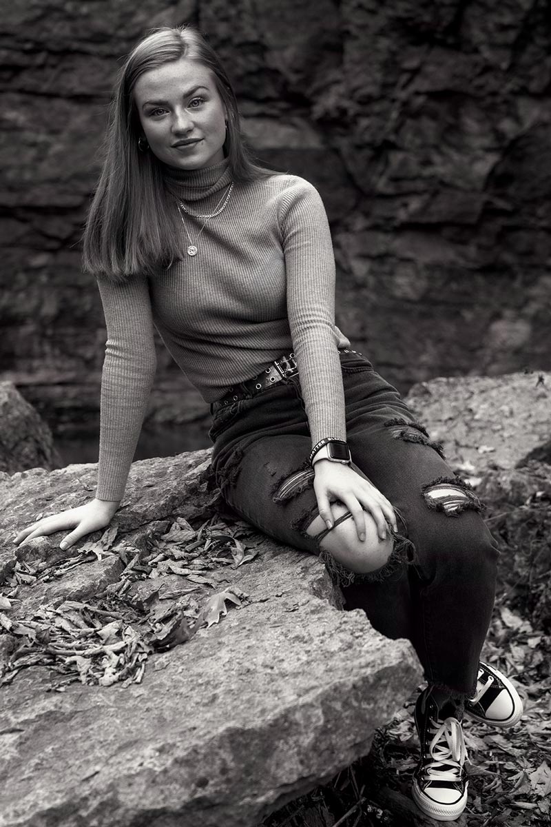 Black and white model photo of a woman sitting on a rock in the woods.
