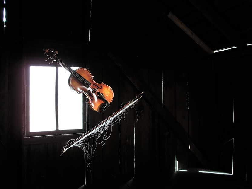 A violin and bow float in front of a window in an old barn.